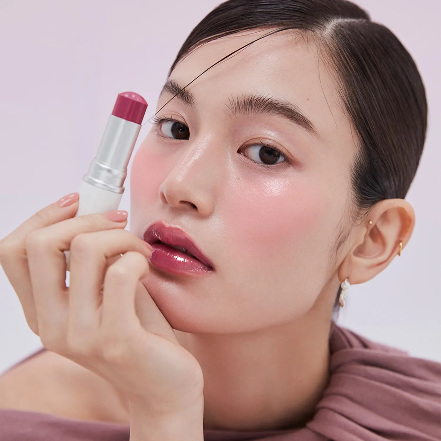 Woman applying lipstick with a pink lip balm on a light purple background